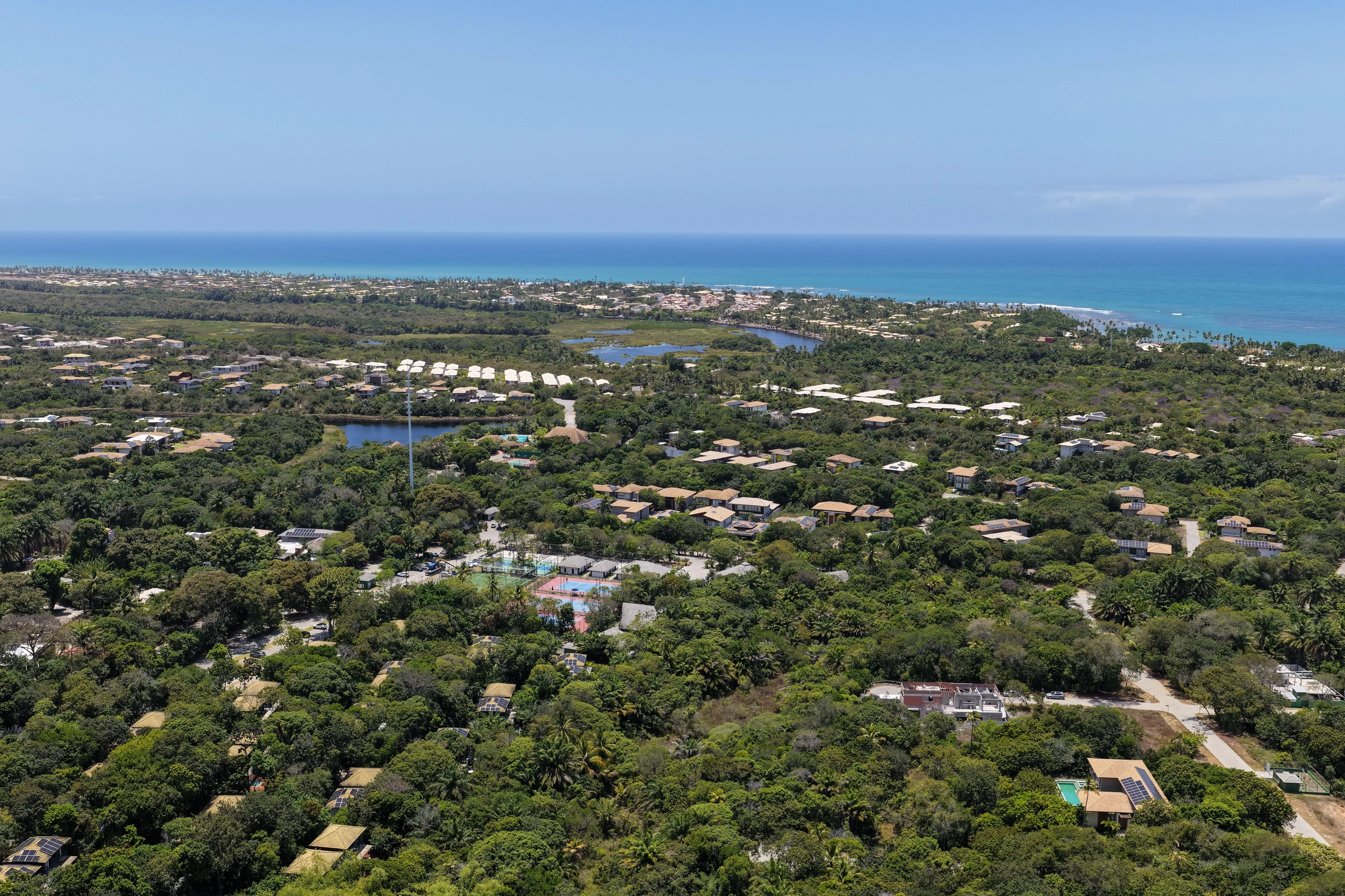 Panorama aéreo aberto do Praia do Castelo, com casas entre a vegetação e o mar ao fundo.