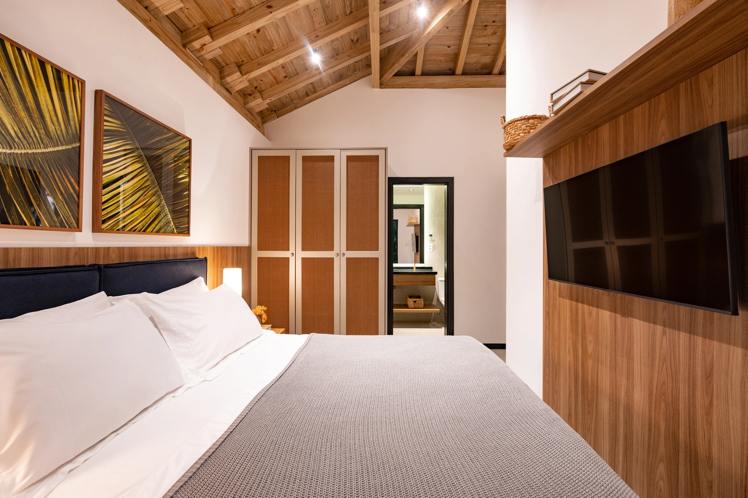 Outra suíte do decorado, com cama clara e acabamento em madeira.