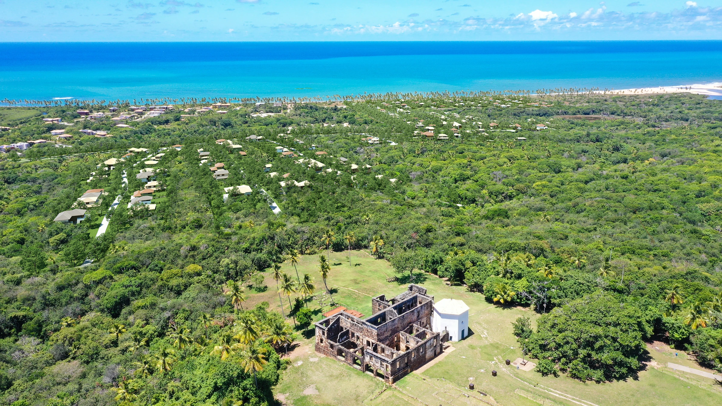 Vista aérea com o Castelo Garcia d’Ávila em primeiro plano, vegetação, condomínio e mar ao fundo.