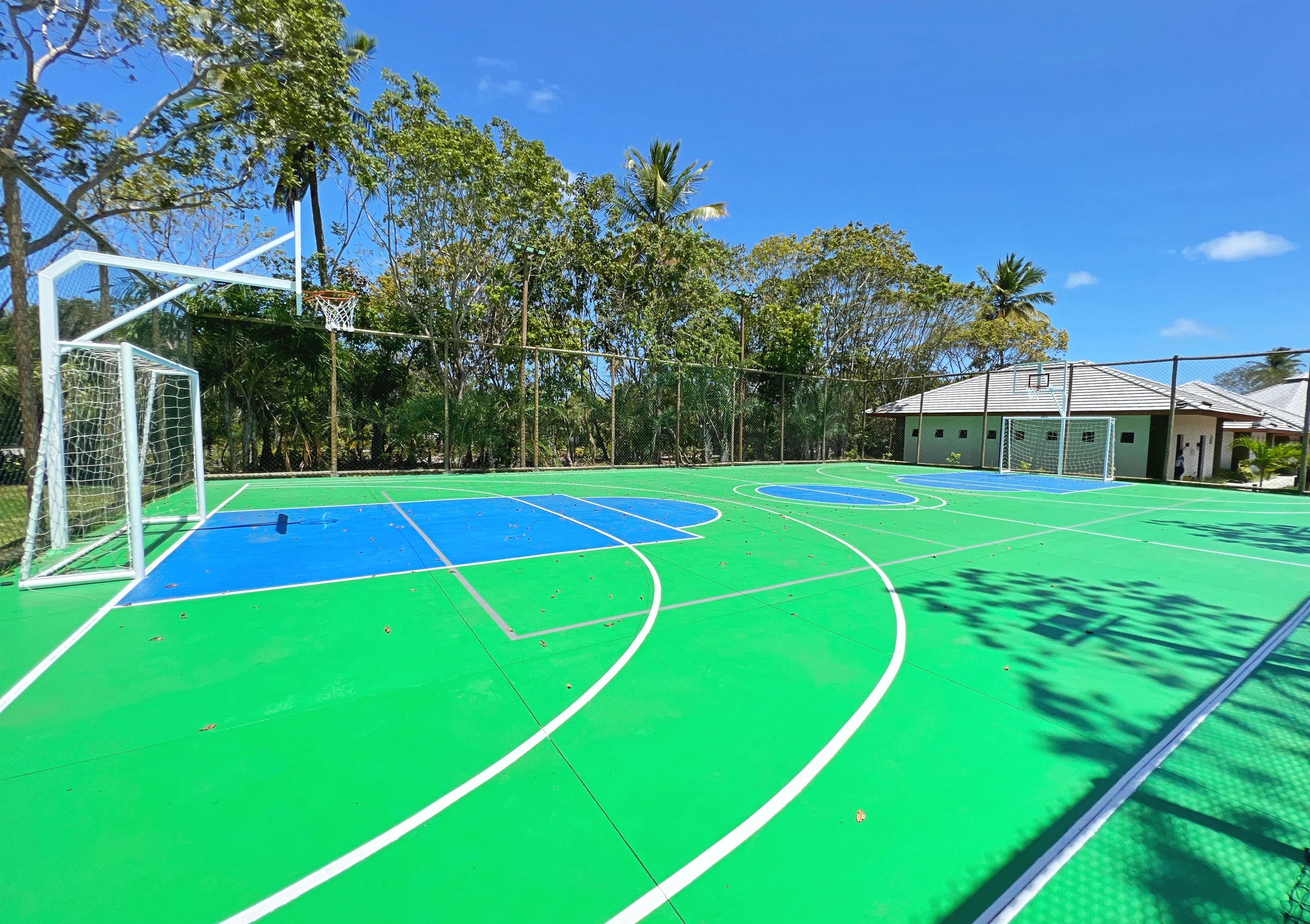 Quadra poliesportiva azul e verde, com traves e cesta de basquete.